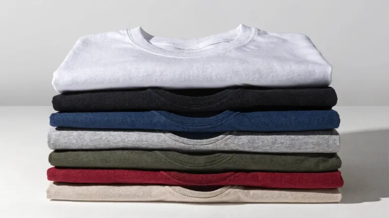 A stack of plain t-shirts in various colors ready for manufacturing.